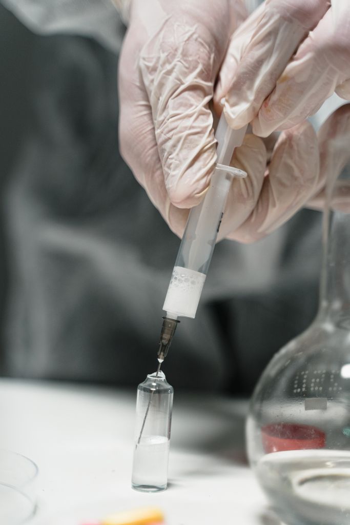 Close-up of hands in gloves using a syringe to extract liquid from a vial in a lab setting.